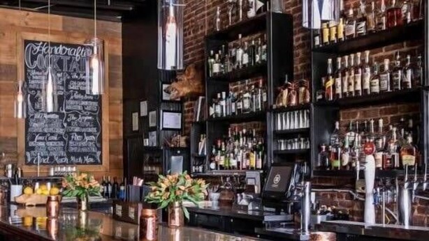 Een bar met een krijtbordmenu, drankflessen op de planken en koperen bekers op de toog.