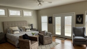 A bedroom with a large bed, two armchairs, a side table, a ceiling fan, and a view of the outdoors through a sliding door. - Lakefront Smith Lake Retreat - Private Dock, Paddleboards, Sleeps 8 (Arley)