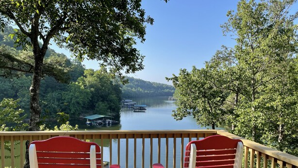 A wooden deck with two red Adirondack chairs facing a lake with boats and docks. - Lakefront Smith Lake Retreat - Private Dock, Paddleboards, Sleeps 8 (Arley)