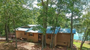 A cabin with a blue roof, surrounded by trees, near a body of water. - Lakefront Smith Lake Retreat - Private Dock, Paddleboards, Sleeps 8 (Arley)