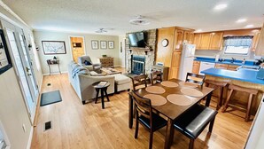 A compact living space with a kitchenette, a dining area with a table and chairs, a sofa, and a television. - Lakefront Smith Lake Retreat - Private Dock, Paddleboards, Sleeps 8 (Arley)