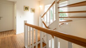 Un escalier en bois avec des rampes blanches mène à une pièce dotée d’une porte et de deux tableaux encadrés accrochés au mur.
