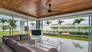 Een moderne woonkamer met een grote bank, een glazen salontafel en een plafondventilator.