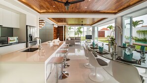 Een moderne keuken met een centraal kookeiland, barkrukken en een eethoek met een glazen tafel en stoelen.