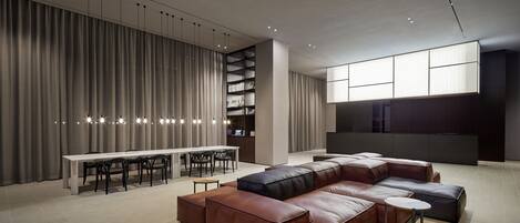 A modern living room with a sectional sofa, a dining table, and a bookshelf.