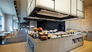 A modern hotel dining area with a buffet setup, seating arrangements, and a large window providing natural light. - Shilla Stay Seobusan (Busan)
