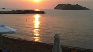 Escena de playa con atardecer, agua tranquila y una isla distante.