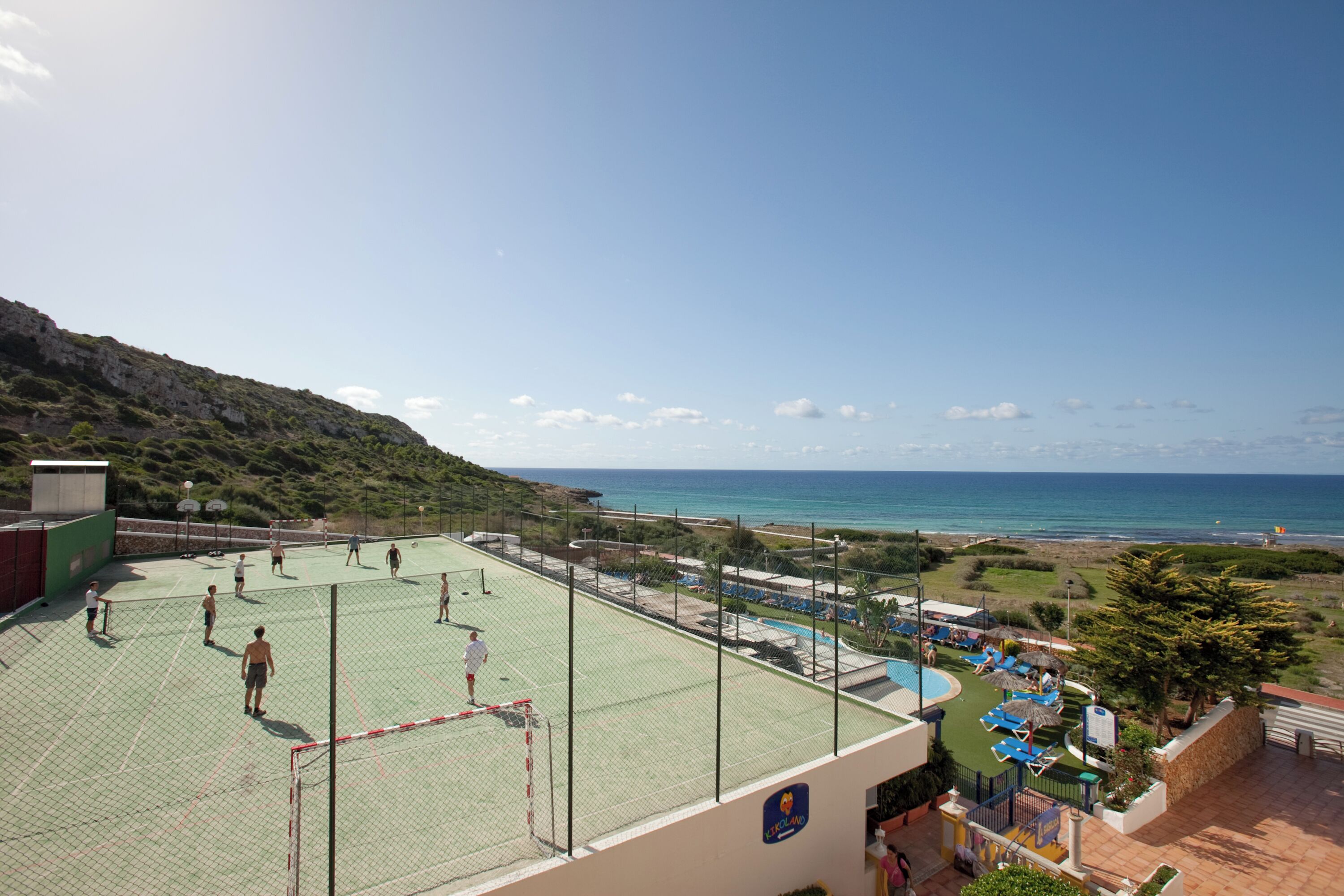 Un campo da tennis con una rete, un'area piscina con lettini e vista sul mare.