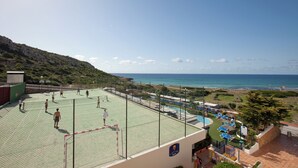 A tennis court with a net, a pool area with lounge chairs, and a view of the sea. - Royal Son Bou Family Club (Alayor)