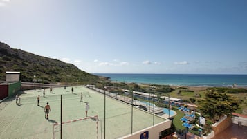 Un campo da tennis con una rete, un'area piscina con lettini e vista sul mare.