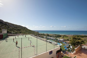 A tennis court with a net, a pool area with lounge chairs, and a view of the sea. - Royal Son Bou Family Club (Alayor)