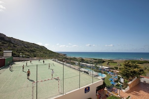 Una cancha de tenis con red, un área de piscina con sillas de descanso y vistas al mar.