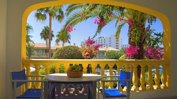 Un balcone con ringhiere gialle, un tavolo con sedie e vista su palme e edifici.
