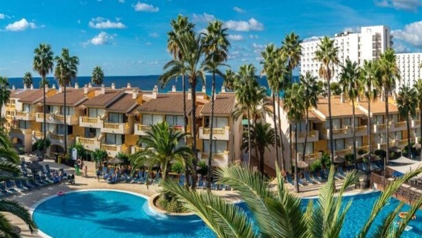 A resort with a large pool, palm trees, and a view of the ocean. - Club Royal Son Bou (Alayor)