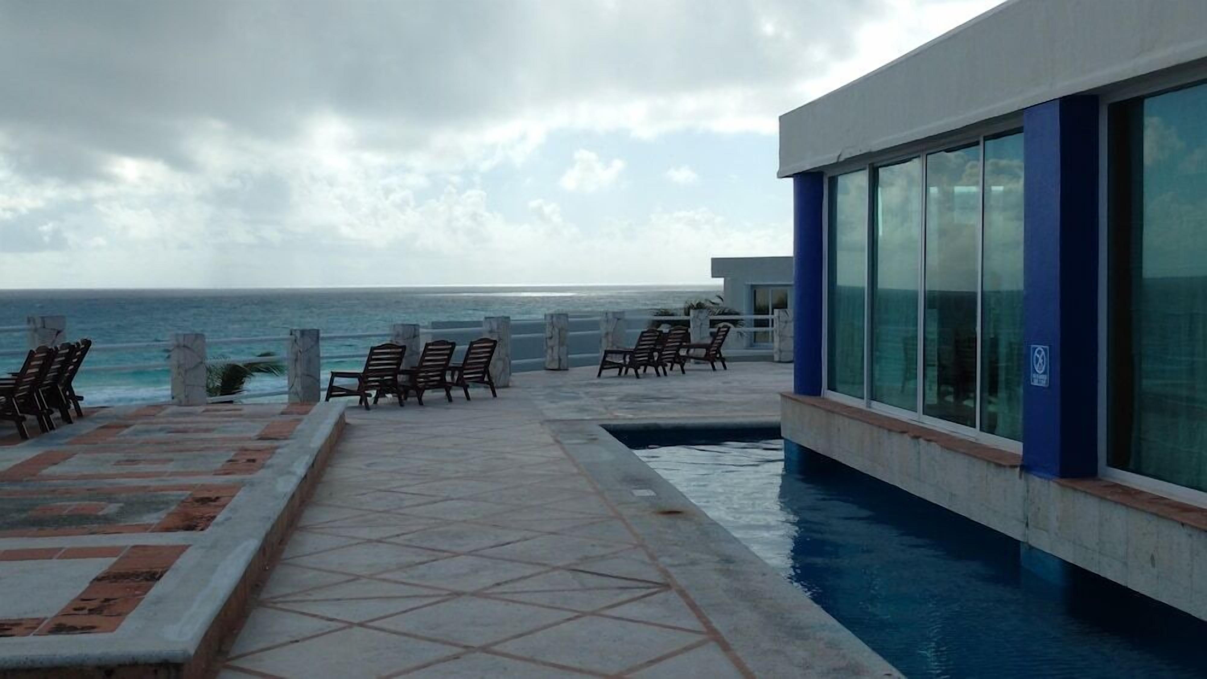 Uma área à beira da piscina com espreguiçadeiras e vista para o mar.