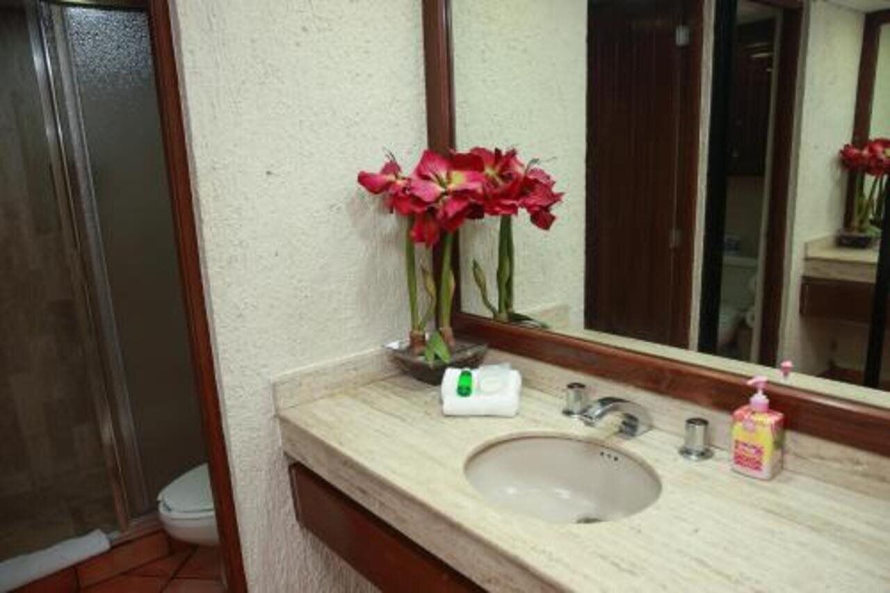 A bathroom with a sink, mirror, and a vase of red flowers.