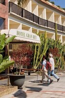 Entrada de hotel con un letrero que dice "HOTEL GRAN REY", una maceta grande con plantas y un camino peatonal.