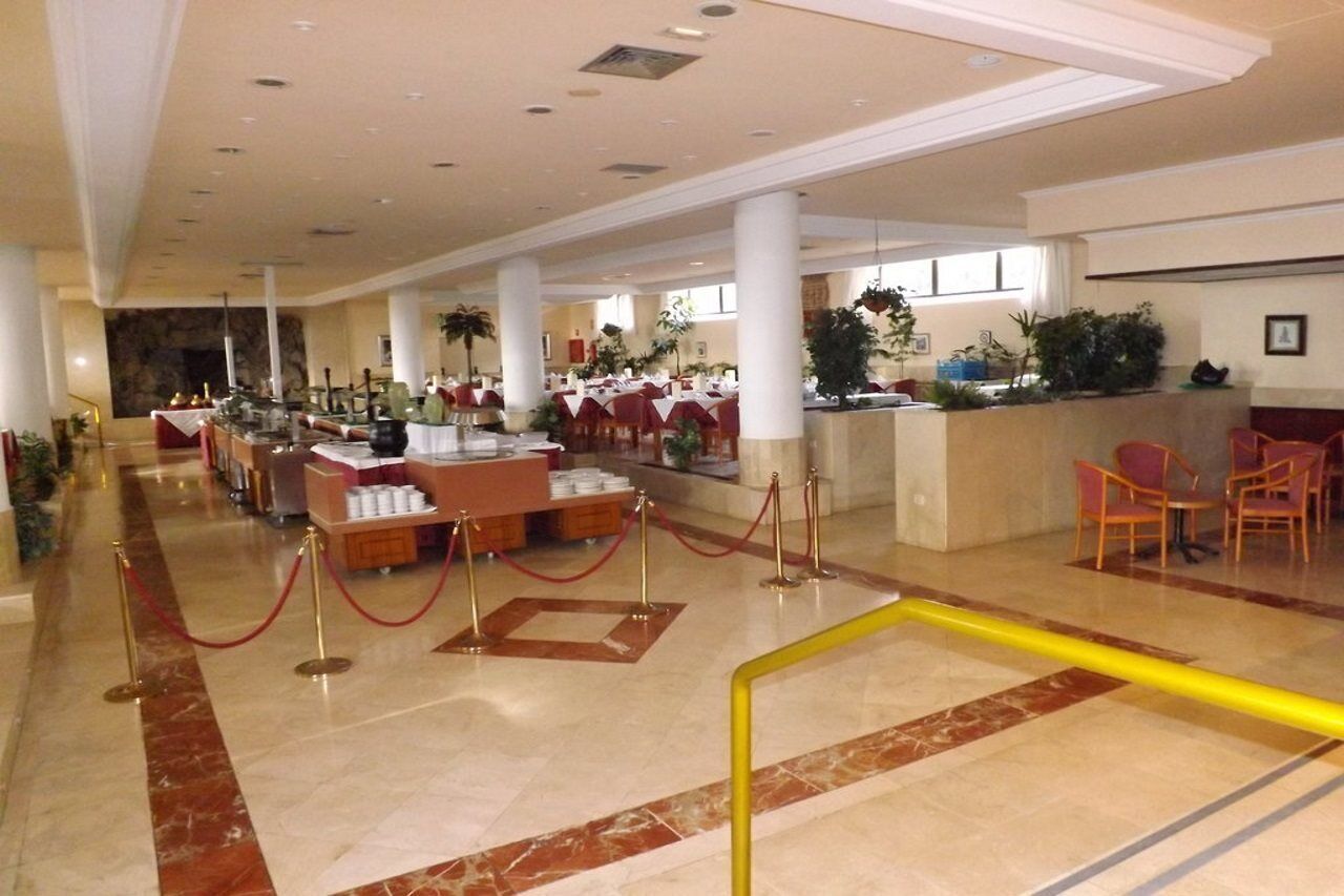 A spacious hotel lobby with marble flooring, a reception desk, and several dining areas with tables and chairs.
