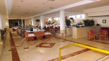 A spacious hotel lobby with marble flooring, a reception desk, and several dining areas with tables and chairs.