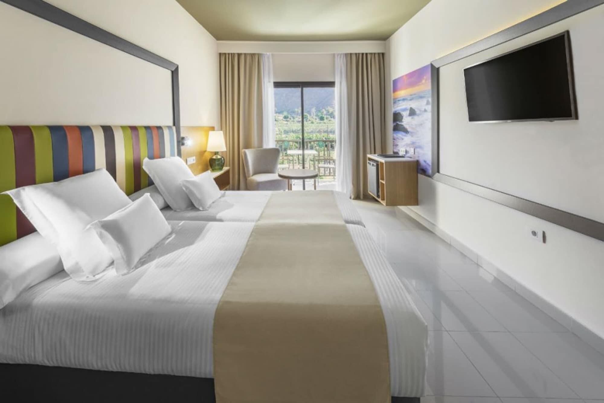 A hotel room with two beds, a TV, a desk, and a balcony view.