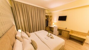 A hotel room with a bed, a desk, a TV, and a bathroom visible through a curtain. - Baron (Tirana)