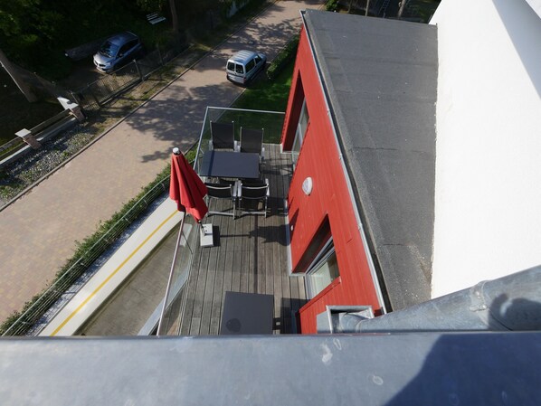 A view from a high vantage point overlooking a building with a red facade, a paved outdoor area with a table and chairs, and a parked car on the street.