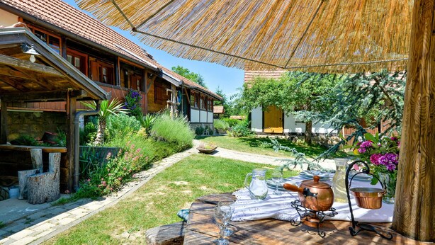 Un espace de restauration en plein air au charme rustique, avec une table en bois dressée pour deux personnes, entourée d’une végétation luxuriante et protégée par un parasol en chaume.