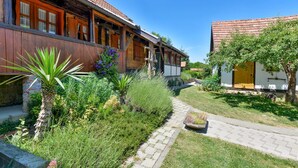 Une maison traditionnelle en bois, avec un toit en tuiles, un chemin pavé et une variété de plantes et d’arbustes dans le jardin.