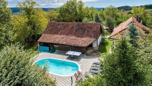 Une maison avec une piscine, entourée d’arbres et située dans un paysage vallonné.
