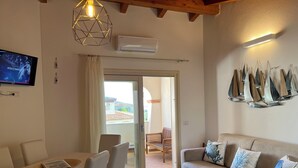 Uma sala de estar moderna com sofá, mesa de jantar e cadeiras. Há uma televisão montada na parede, um lustre e um ar condicionado fixado na parede.