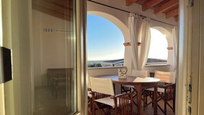 Uma varanda com mesa e cadeiras de madeira, cortinas brancas e vista para a paisagem.