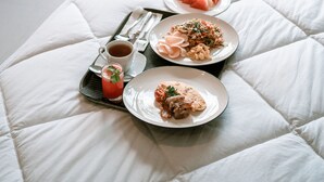 A bed with a tray of breakfast including toast, eggs, and a drink, with a view of a garden and outdoor seating. - One Degree Sunset Hill Leisure (Pecatu)
