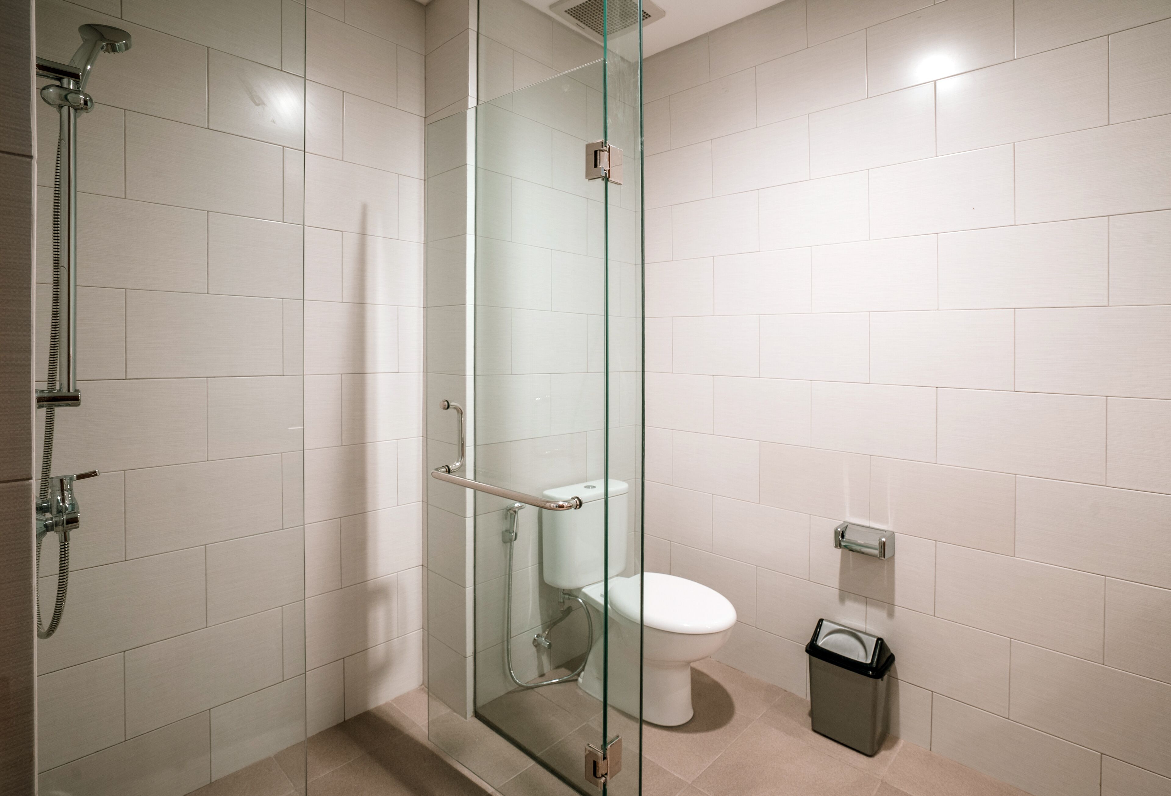 Un baño moderno con ducha envuelta en vidrio, inodoro y contenedor de basura.