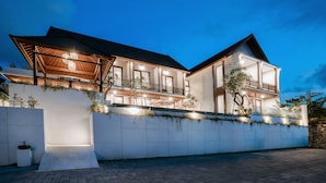 A modern two-story house with a large balcony, a covered patio, and a stone retaining wall. - One Degree Sunset Hill Leisure (Pecatu)