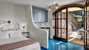A bedroom with a curved wall, a bed, a nightstand, and a view of a patio with outdoor furniture. - Appartamento Lobra (Massa Lubrense)