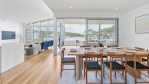 A modern dining area with a wooden table and chairs, a television, and a view through large windows.