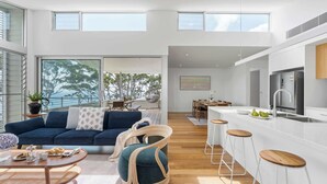 A modern interior with a sofa, chairs, a dining table, a kitchen with a bar, and large windows.