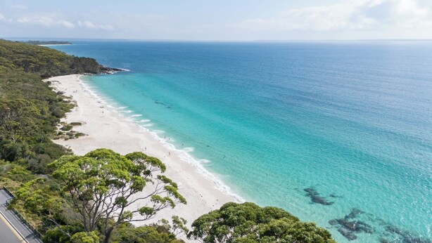 A beach with clear turquoise water, a sandy shore, and dense green foliage.