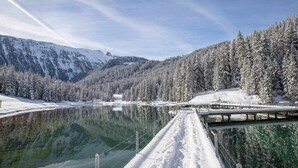 A snow-covered landscape with a lake, a wooden bridge, and a forested mountain backdrop. - Courchevel 1850: 2-room flat, south-facing balcony, parking (Courchevel 1850)