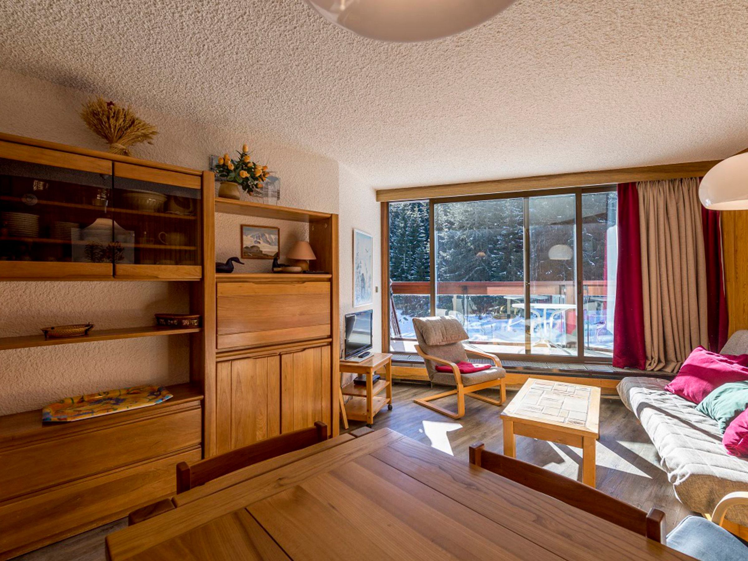 Ein gemütliches Wohnzimmer mit Holzmöbeln, einem großen Fenster mit Blick auf Bäume und einem Kamin.