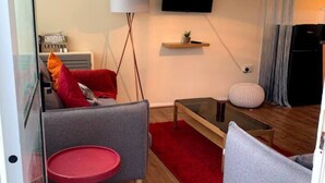 A modern living room with a sofa, a small round table, a television mounted on the wall, and a red rug on the floor. - Cosy and Modern 2-bed House in Great Yarmouth (Great Yarmouth)