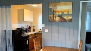 A dining area with a wooden table and chairs, a yellow pendant light, and a painting on the wall. - Cosy and Modern 2-bed House in Great Yarmouth (Great Yarmouth)