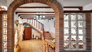 A spacious dining area with a wooden table and chairs, a brick archway, and a staircase leading to an upper level.