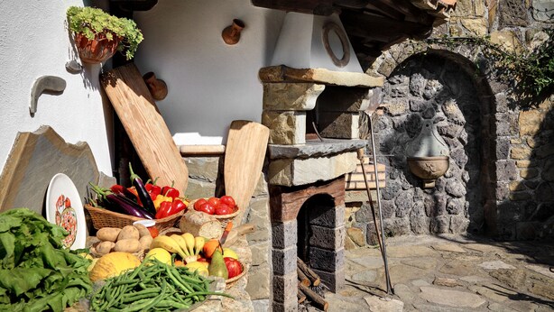 A rustic outdoor setting with a stone oven, fresh produce, and a wooden table.