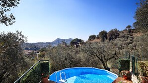 An outdoor swimming pool with a wooden deck, lounge chairs, and a view of a mountainous landscape.