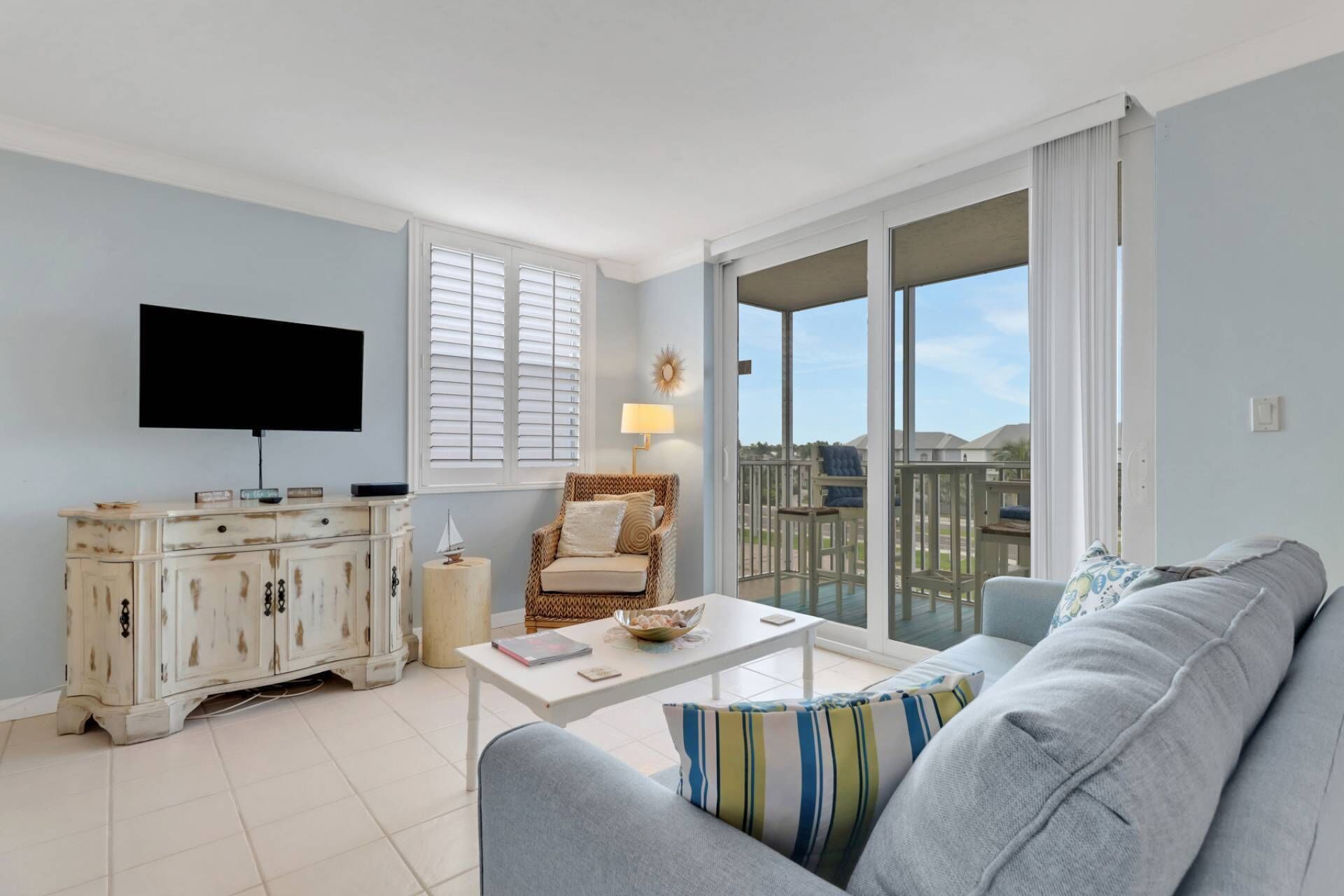 A living room with a sofa, a coffee table, a TV, a wicker chair, and a balcony with a view.