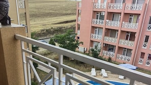 A balcony with a pool, lounge chairs, and a view of a pink building with balconies. - Stunning 1-bed Apartment in Sunny Beach (Nessebar)
