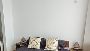 A neatly made bed with a dark patterned bedspread and two decorative pillows, a wooden nightstand with a lamp, and a wooden floor. - Stunning 1-bed Apartment in Sunny Beach (Nessebar)