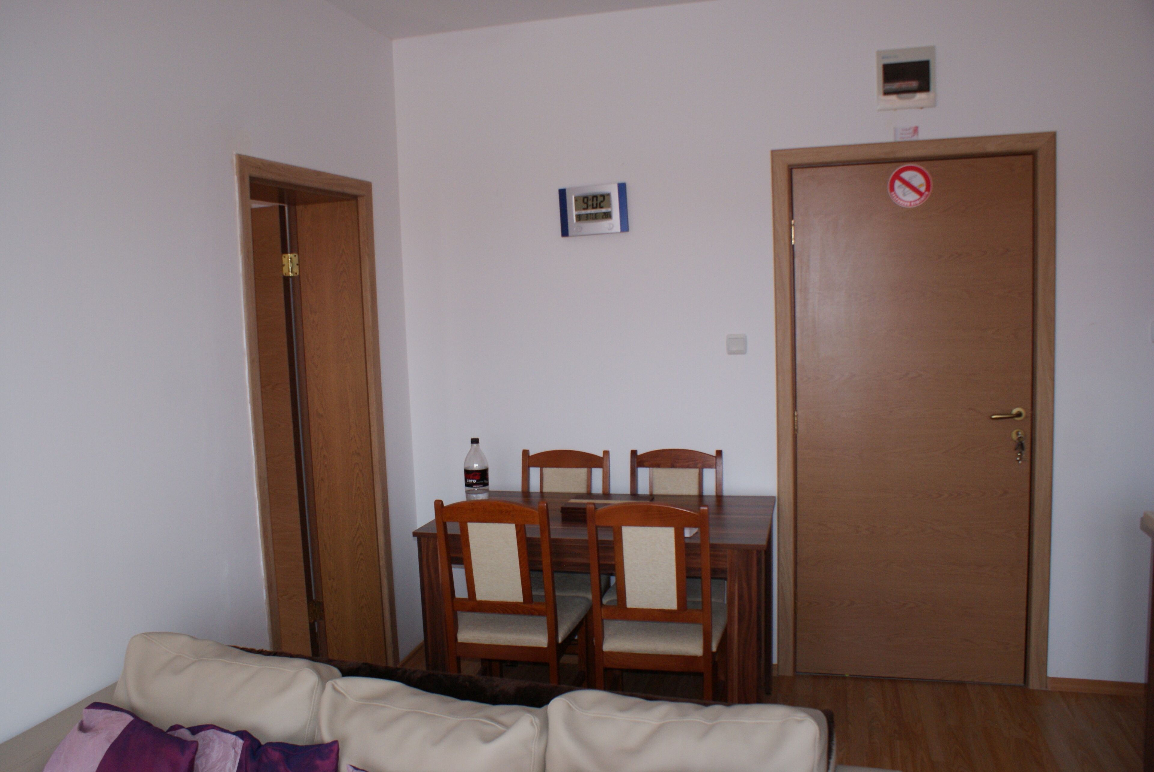 A dining area with a wooden table and chairs, a clock on the wall, and a closed door with a no entry sign.