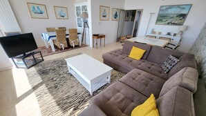 A modern living room with a sofa, coffee table, TV, and framed artwork on the walls. - Elegant Apartment with Balcony, Garage and WiFi by the Sea (Les Sables-d'Olonne)